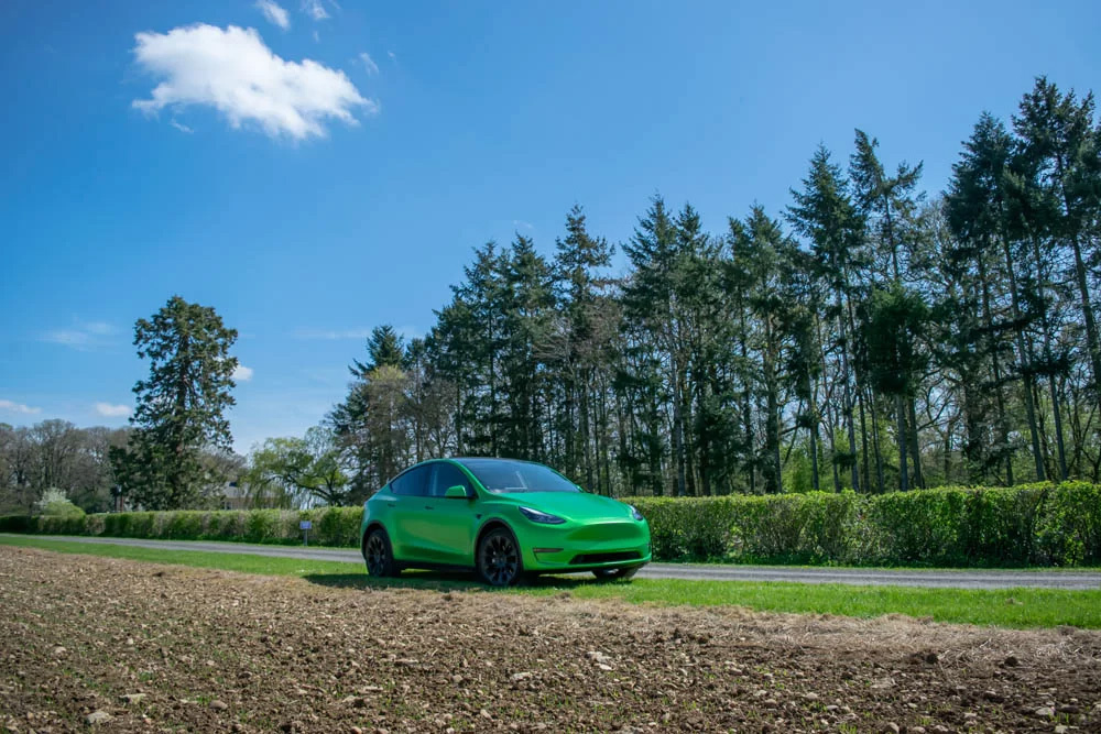 A green car parked on a road surrounded by trees, showcasing a serene outdoor setting.