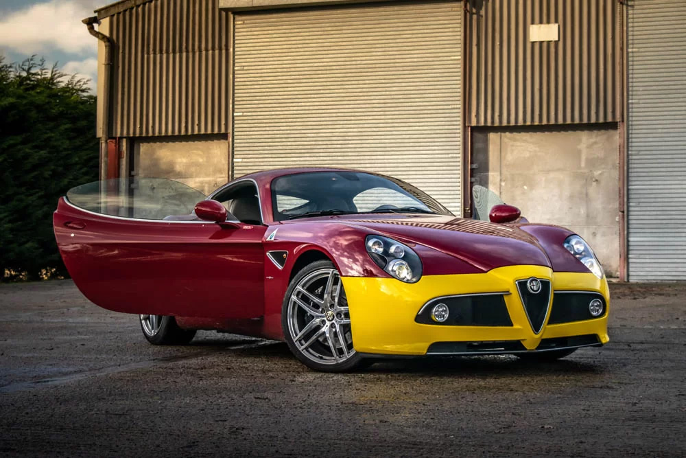 A red and yellow sports car parked in front of a garage, showcasing its sleek design and vibrant colors.