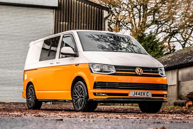 A Volkswagen Transporter parked in front of a rustic barn, showcasing its sleek design against a rural backdrop.