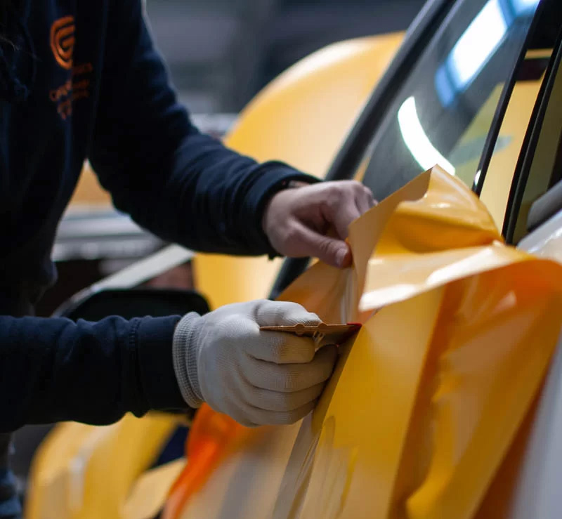A man is painting a car with yellow paint, focused on applying an even coat.