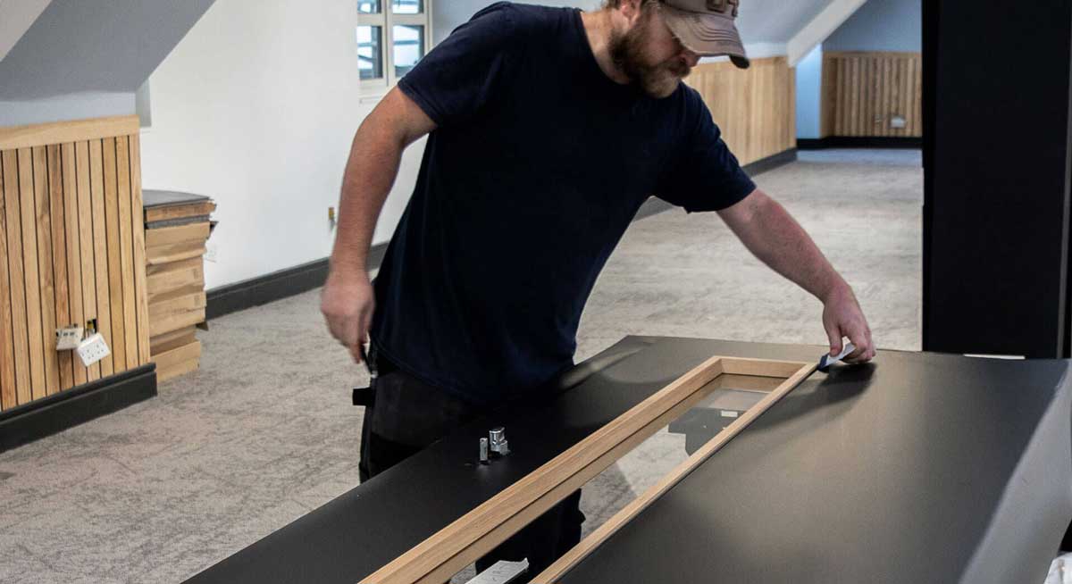 A man is focused on a task at a table with a sleek black surface, surrounded by tools and materials. 