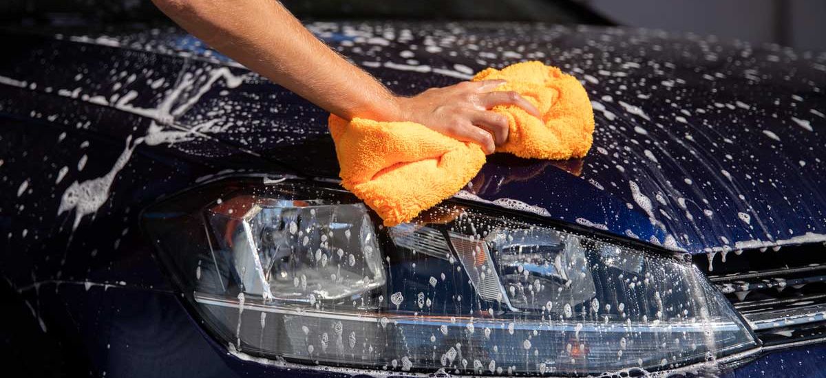 A person diligently washes a car using a sponge, ensuring a thorough clean and shine on the vehicle's surface.