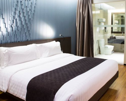 A neatly made bed in a stylish hotel room, featuring crisp white linens and decorative pillows. 