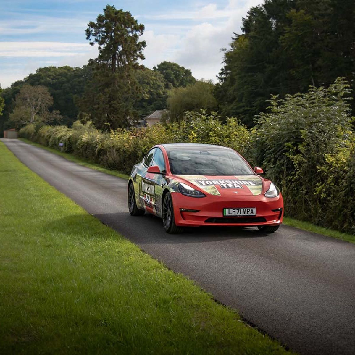 Red Tesla Model 3 with Yorkshire Tea vehicle wrap driving along a country road.