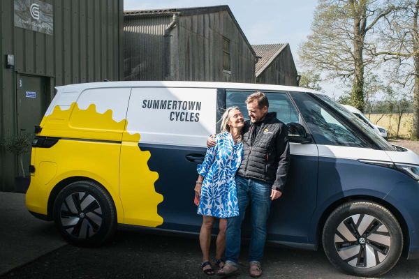 A man and woman stand beside a van with a bicycle mounted on the back, ready for an outdoor adventure.  