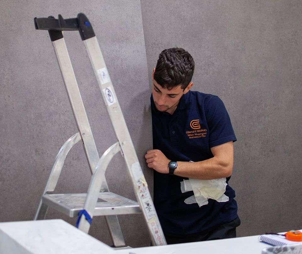 Man wrapping a wall with grey wallpaper.
